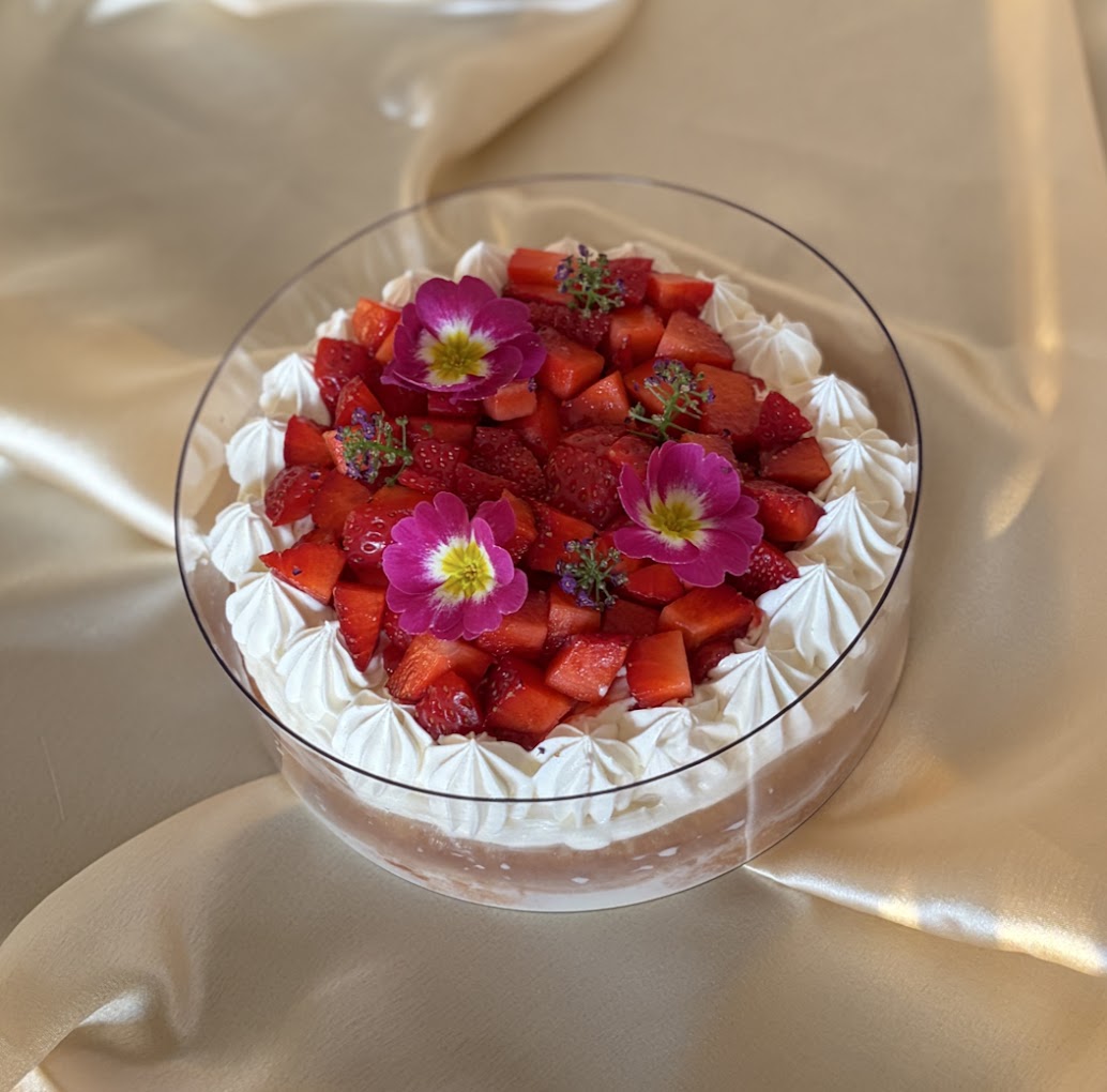 Strawberry Tres Leches topped with whipped cream, fresh strawberries, and edible flowers